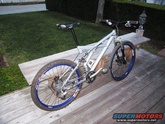 Silver full-suspension mountain bike with blue rims on a wooden deck