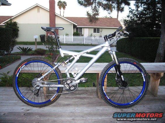 Silver full-suspension mountain bike with blue rims on a wooden deck