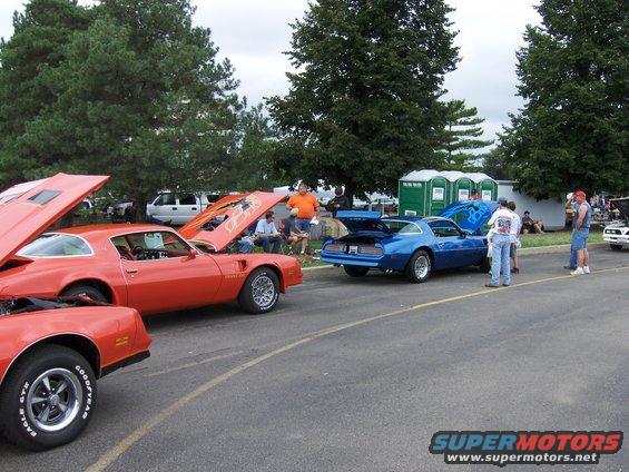 Orange and blue 1977 Pontiac Trans Ams parked on asphalt with hoods open