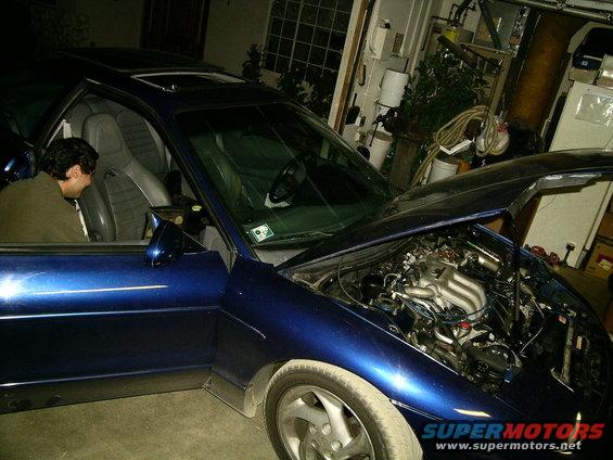 Blue coupe with hood open, showing engine. Door is open with a person inside. Visible text: SUPERMOTORS.NET