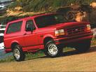 Red 1996 Ford Bronco parked on a dirt road near some rocks and vegetation