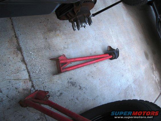 Two red suspension control arms and a vehicle's brake rotor and hub assembly on a concrete surface