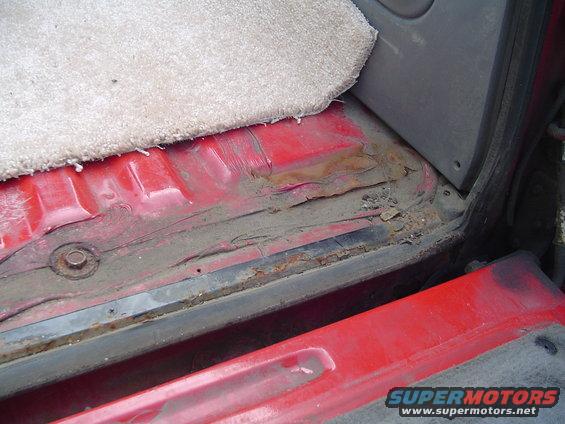 rusted red metal floor panel with carpet edge and visible bolt