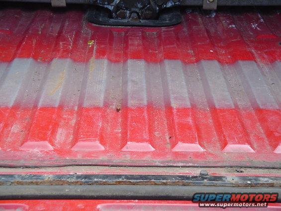 Red truck bed with white spray-on liner showing wear