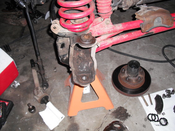 Vehicle's front suspension and brake parts laid out on the floor next to a jack stand holding up the knuckle