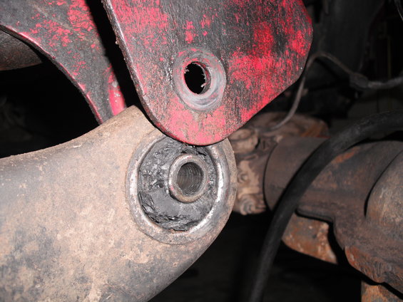 Close-up of a worn suspension bushing in a red bracket, showing damage to the rubber