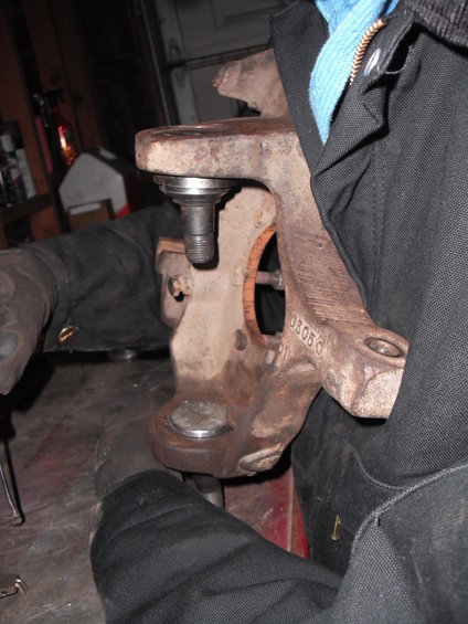 Close-up of a rusty ball joint assembly being held by gloved hands