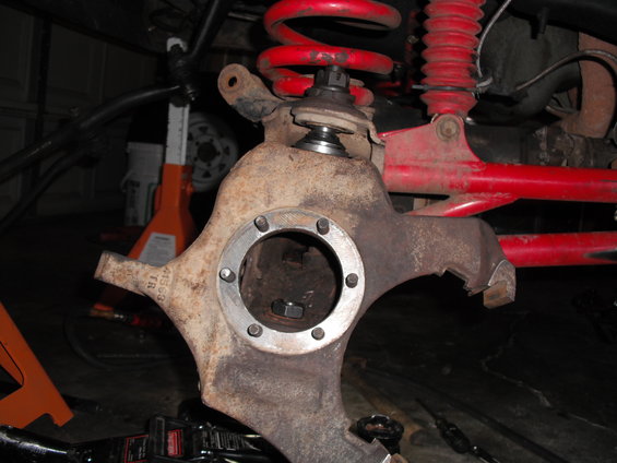 Rusty suspension knuckle with red coil spring and shock absorber above