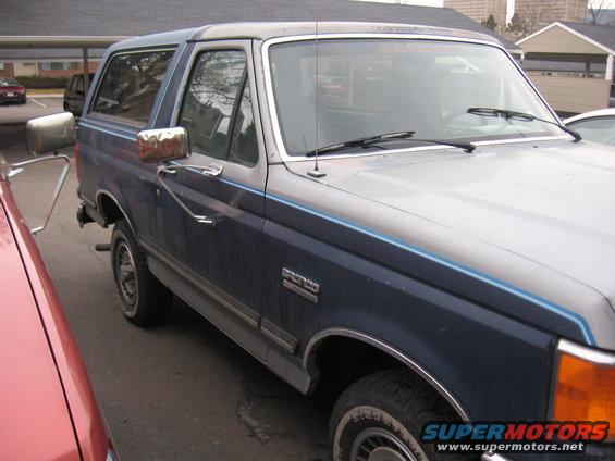 Blue and silver 1987 Ford Bronco parked next to a red car