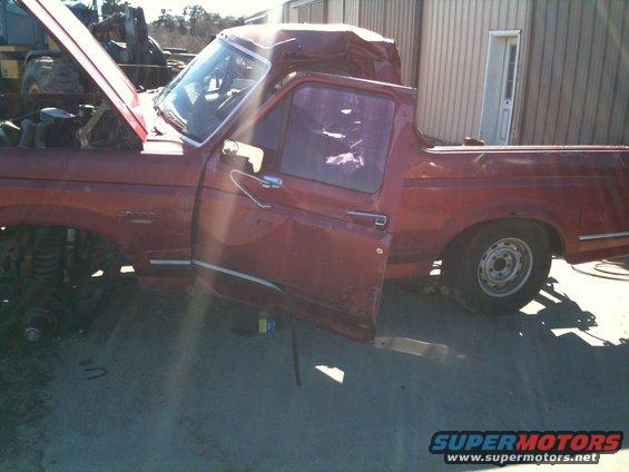 Red 1993 Ford Bronco with damaged roof and open door