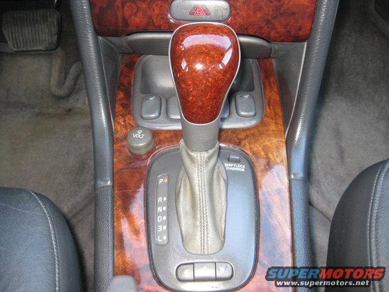 Car interior showing automatic transmission shifter, wood trim, and 12V power outlet