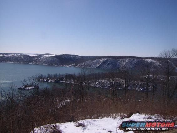 Winter landscape with a lake and snow-covered hills under a clear blue sky