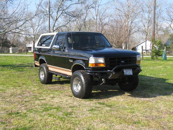 Black 1994 Ford Bronco with tan stripe and white top, lifted with off-road tires