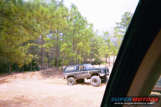 lifted black SUV with large tires parked on dirt road, trees in background
