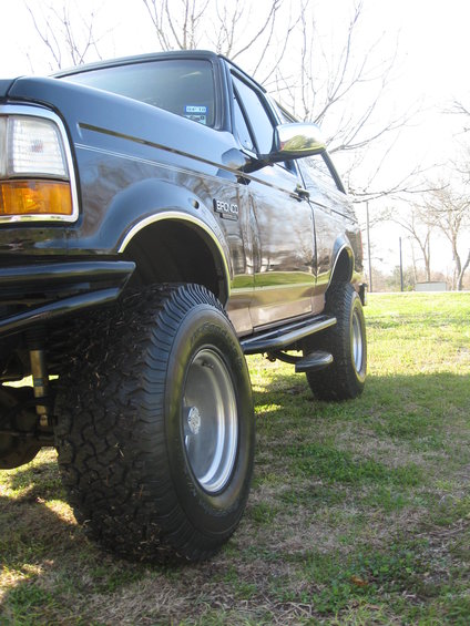 Black Ford Bronco, lifted with large tires. Side view showing front fender and door