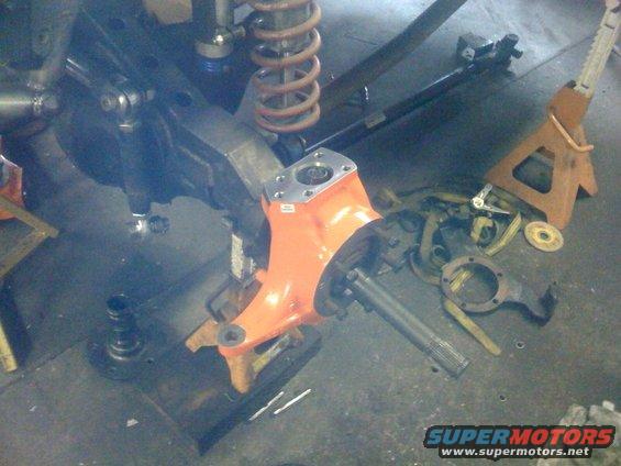 Orange-painted axle housing and suspension parts on jack stands
