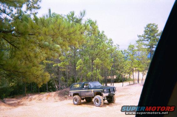 Dark green SUV with large tires and a brush guard, parked on a dirt road