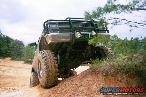 Off-road SUV with large tires climbing a dirt hill, front bull bar visible