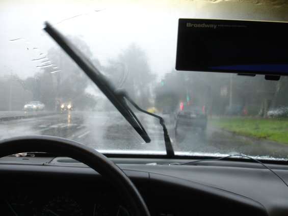 Interior view of car driving in rain, windshield wipers active, "Broadway" device visible