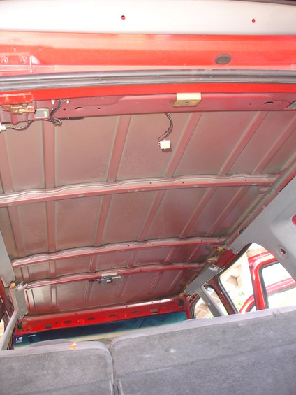 Interior view of a vehicle's red painted ceiling structure with exposed metal ribs and wiring