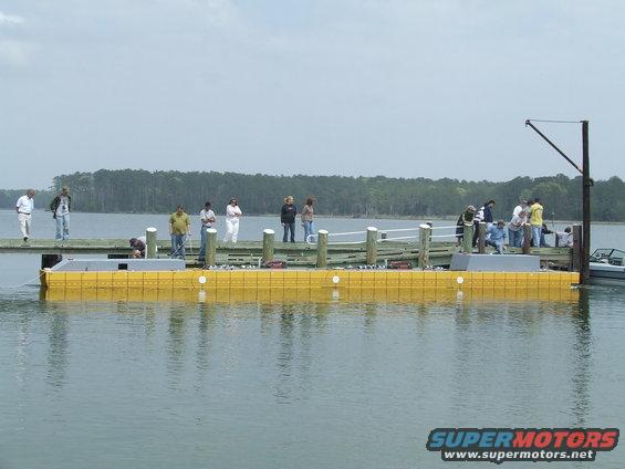 People stand on a wooden dock next to a yellow floating structure in the water