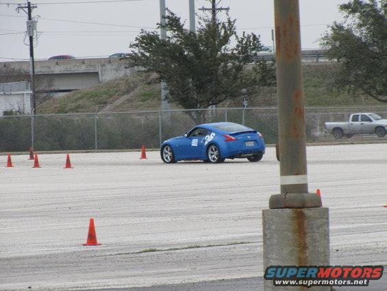 Blue sports car with number 26 on door, seen from rear-right angle on a track with orange cones