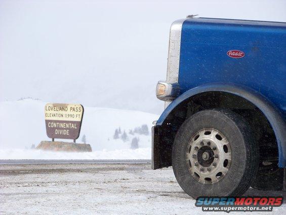 Blue semi-truck, front wheel and fender visible, parked near a sign for Loveland Pass Continental Divide