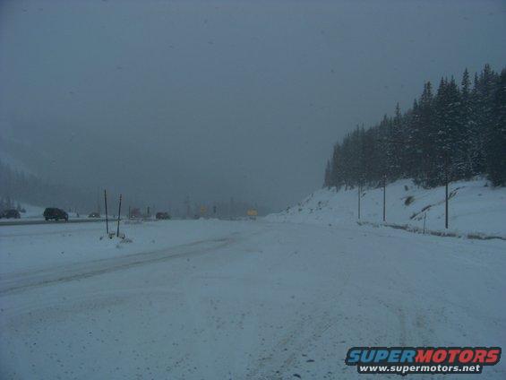 Snowy mountain road with several vehicles driving in low visibility conditions