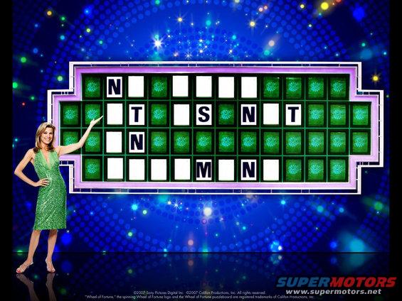 Woman in green dress points to Wheel of Fortune puzzle board with letters N, T, S, M visible