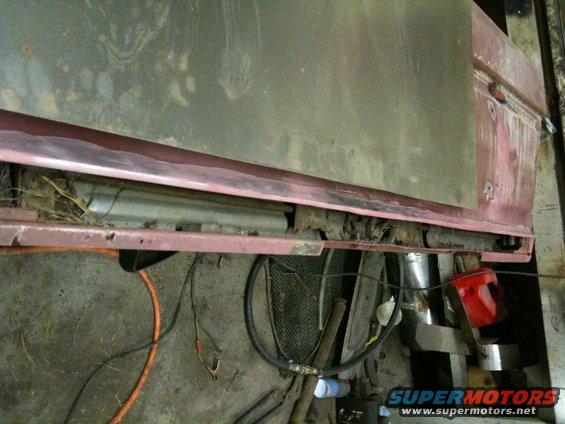Close-up of rusted metal body panel and undercarriage of a vehicle, with wires and a red object visible