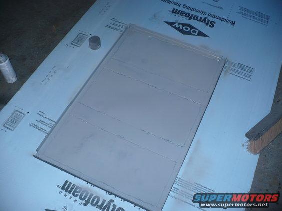 Gray painted panel with horizontal lines, sitting on Styrofoam insulation board. Spray can and brush nearby