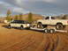 1995 Ford Bronco - A white pickup truck is being towed by another pickup truck on a trailer in a dry, dusty area.
