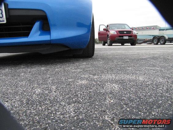 Low angle of blue car's front bumper and tire, red SUV with open door in background