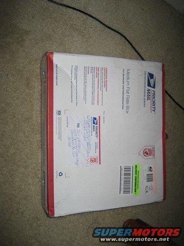 USPS Priority Mail box with handwritten address and shipping labels, on carpet