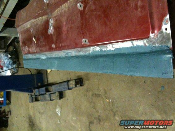 Red car door panel with blue primer applied to lower section, undergoing repair