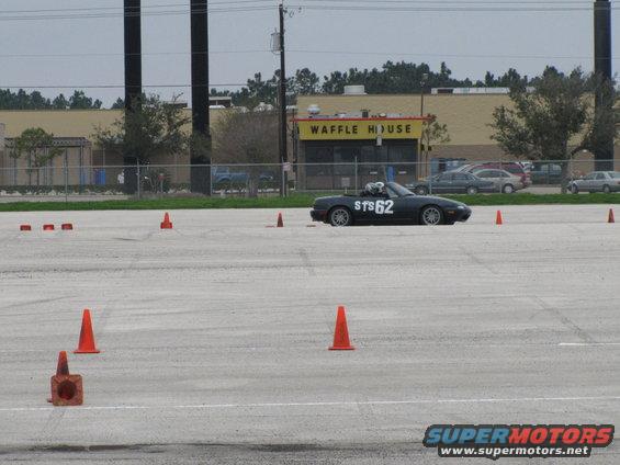 Black convertible sports car with STS 62 on the side, on a paved lot with cones
