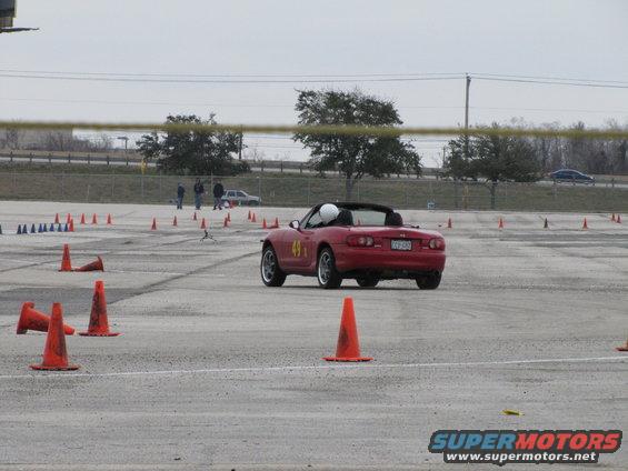 Red convertible sports car with number 49 on the door, driving on a track with orange cones