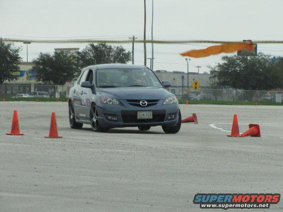 Blue hatchback car with a license plate reading DCM-748, seen from the front on a paved surface with orange cones