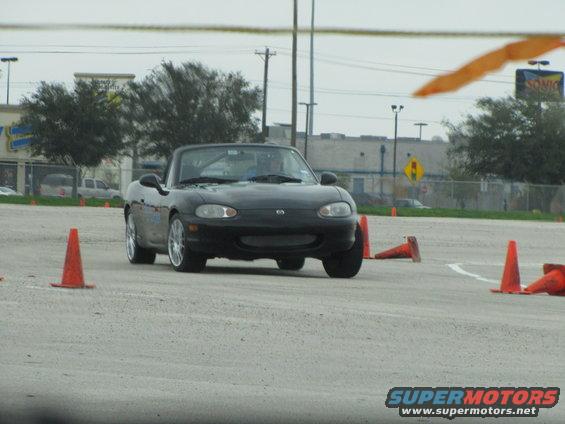 Black convertible sports car with a soft top, viewed from the front at an autocross event