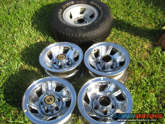 Four chrome wheels with gold center caps and one Goodyear tire on grass