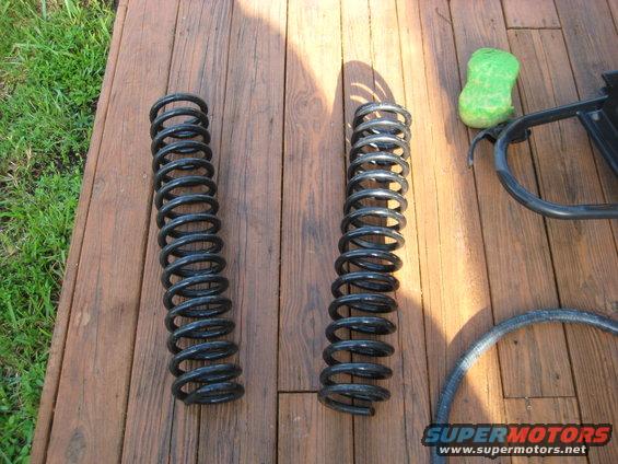 Two black coil springs on a wooden deck, with a green sponge and part of a black frame visible