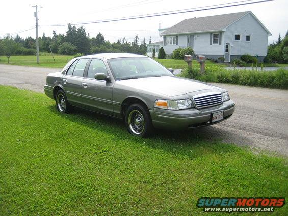 Gray Ford Crown Victoria parked on grass, front 3/4 view. License plate visible