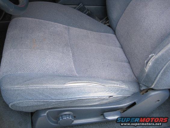 Gray fabric driver seat with torn bolster and visible adjustment knob