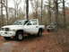 2001 Dodge 1500 - A muddy white 2001 Dodge 1500 pickup truck is parked in a forest, with another dark truck visible in the background.