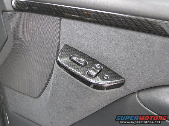 Close-up of a car's interior door panel with carbon fiber trim around the window controls