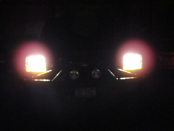 Vehicle front with headlights on at night. Two round fog lights are visible below the headlights
