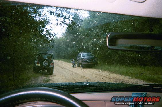 Two SUVs on a dirt road, one is a Jeep Wrangler, the other appears to be a Chevrolet Tahoe