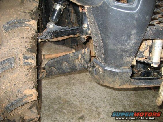 Close-up of an ATV's front suspension, shock, and knobby tire covered in mud
