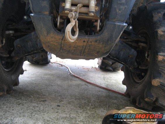 Underside of an ATV showing the winch, hook, and front suspension. A red cable runs across the ground