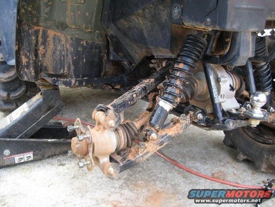 Close-up of ATV rear suspension and hitch assembly, with one wheel removed and a jack underneath